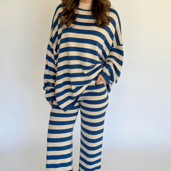 A person wearing a matching two-piece loungewear set with blue and cream horizontal stripes, featuring a long-sleeve top and wide-leg pants, standing against a plain light background.