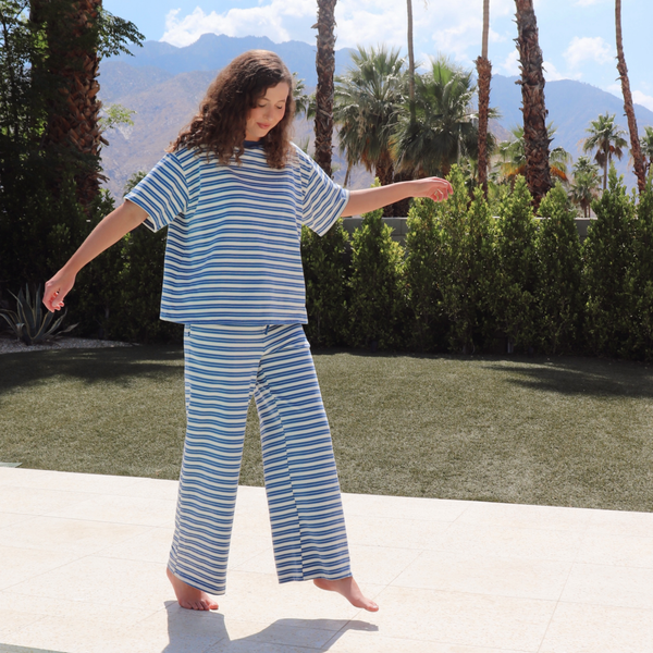 Person wearing blue and white striped set standing outdoors with palm trees and mountains in the background