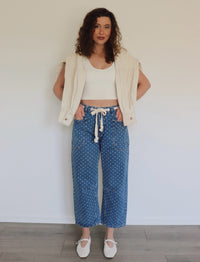 woman wearing white tank top and blue jeans with white polka dots on them against a white wall