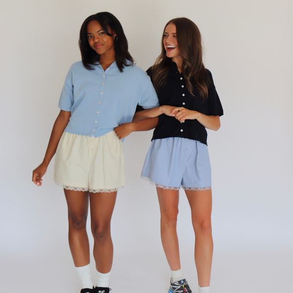 Two women standing side by side wearing matching outfits with a plain background