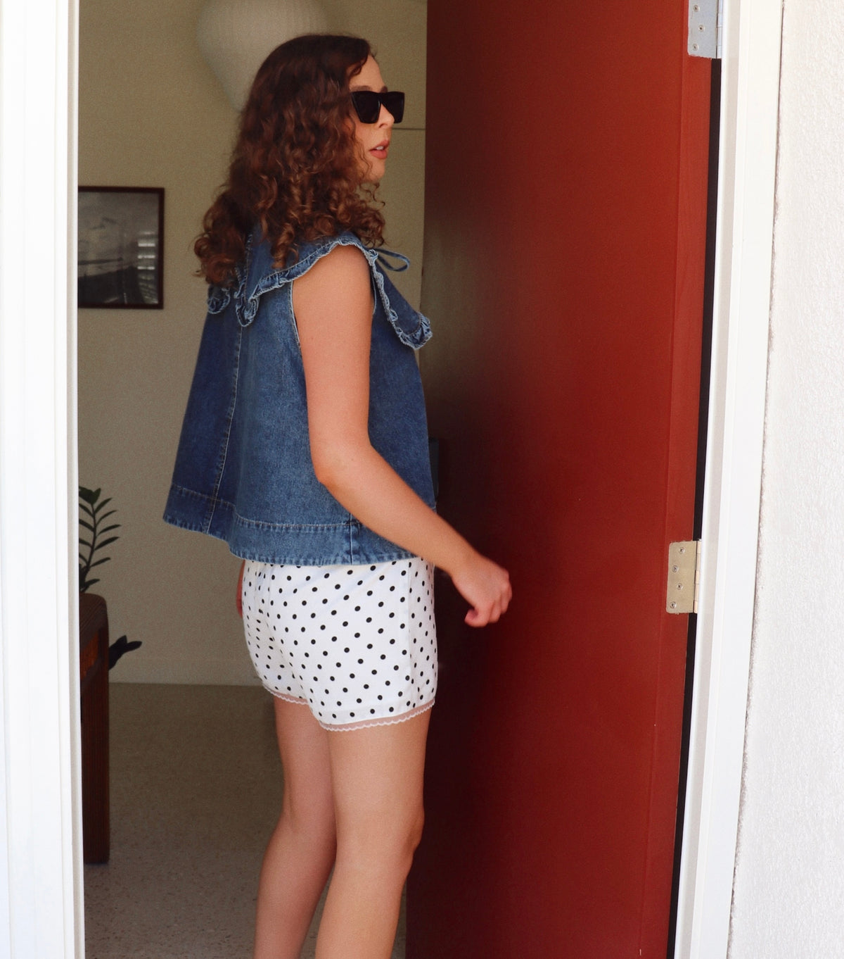 Woman wearing a denim top and polka dot shorts standing in a doorway.