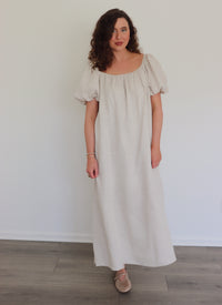 Woman wearing a long beige linen dress against a white wall