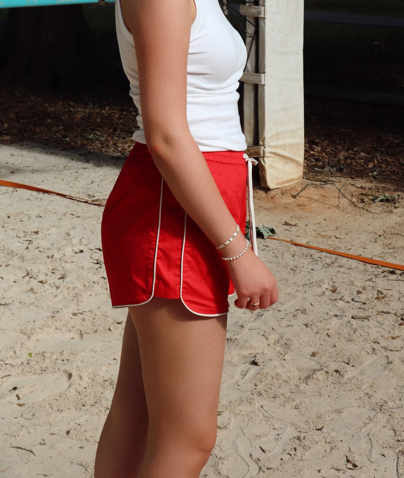 Woman in white tank top and red shorts standing on a sandy surface