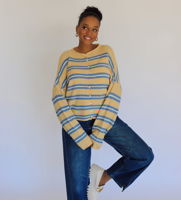 Person wearing a yellow and blue striped cardigan with blue jeans against a white background