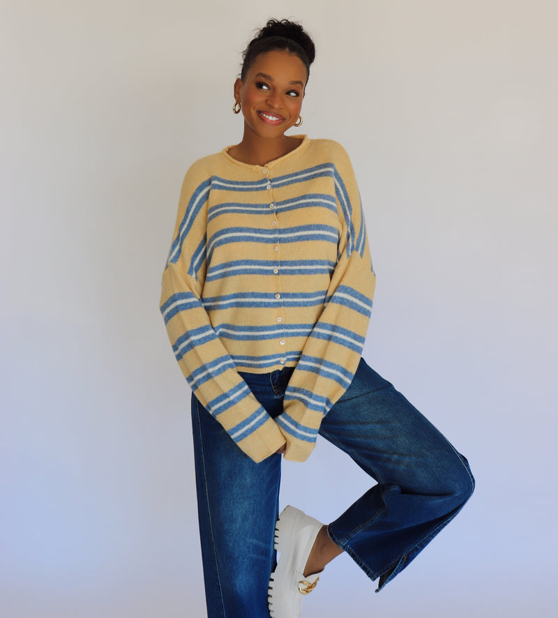Person wearing a yellow and blue striped cardigan with blue jeans against a white background