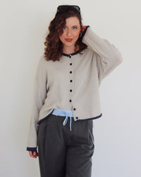 Woman wearing a gray cardigan with blue buttons and gray pants against a white background