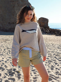Woman wearing a beige sweater with a fish design and checkered shorts on a beach.