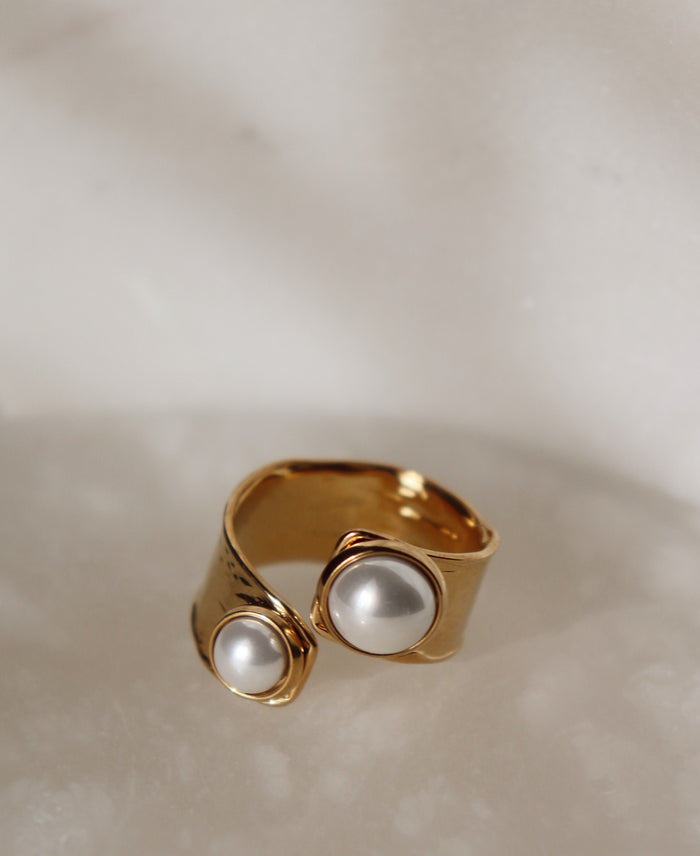 Gold ring with two pearl style details on a neutral background