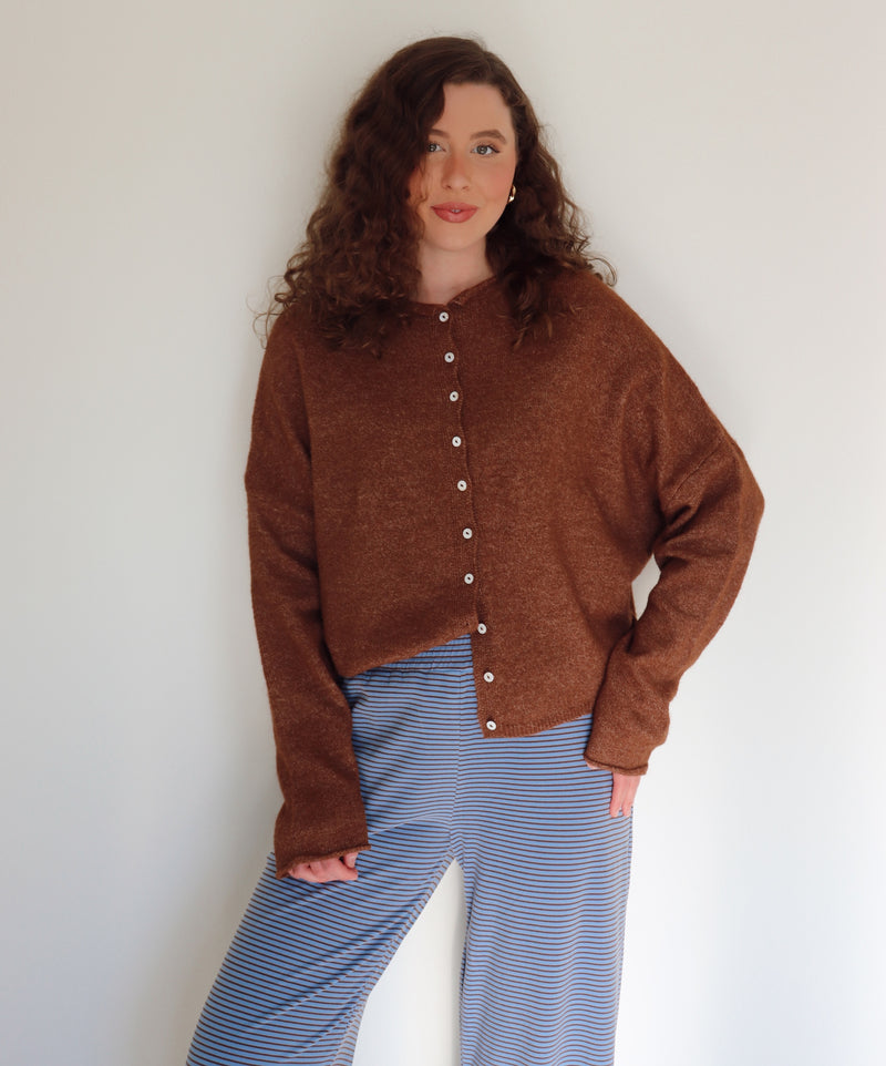 Woman wearing a brown cardigan over blue and brown striped pants against a plain background.