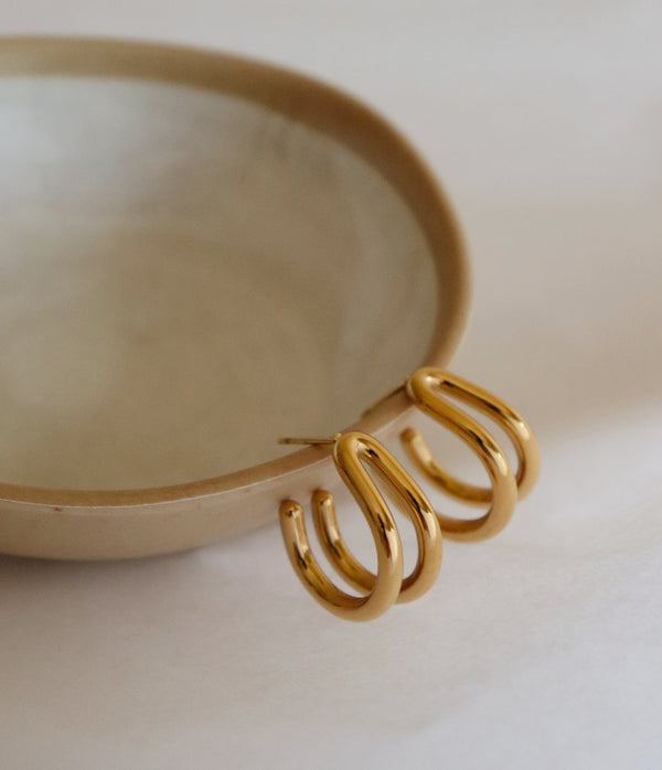 Gold hoop earrings on a beige dish with a neutral background