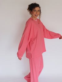 A woman modeling a matching pink striped lounge set, featuring a long-sleeve top and wide-leg pants, against a plain white studio background.