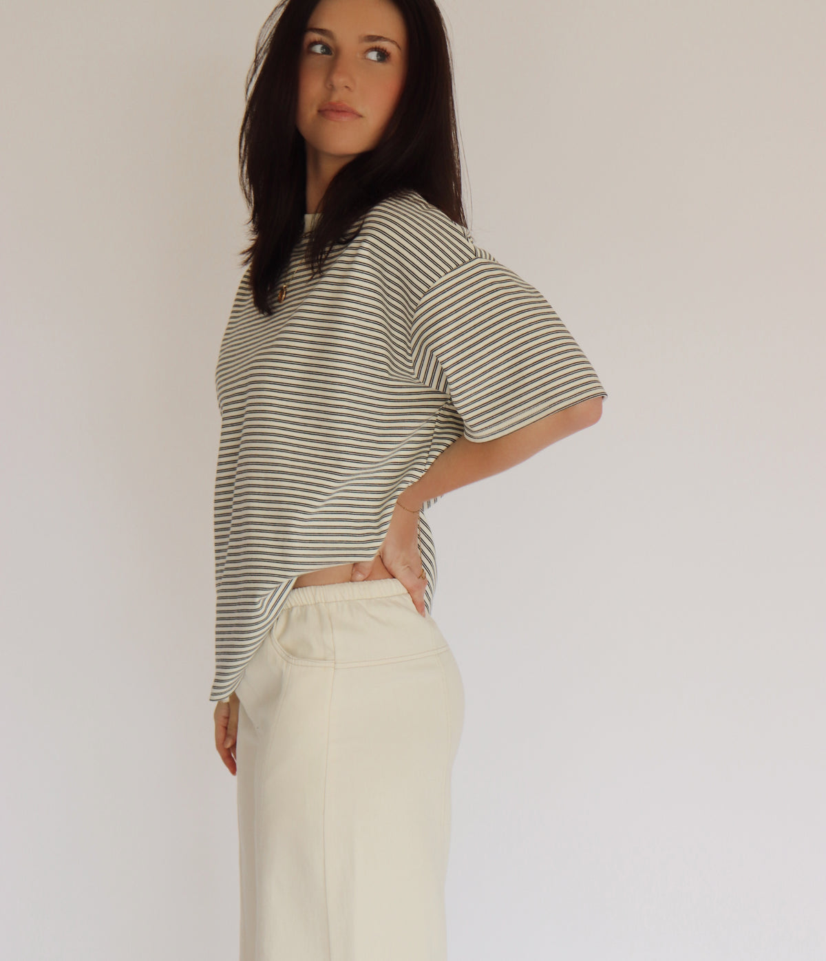 Woman wearing a striped shirt and cream pants against a plain background