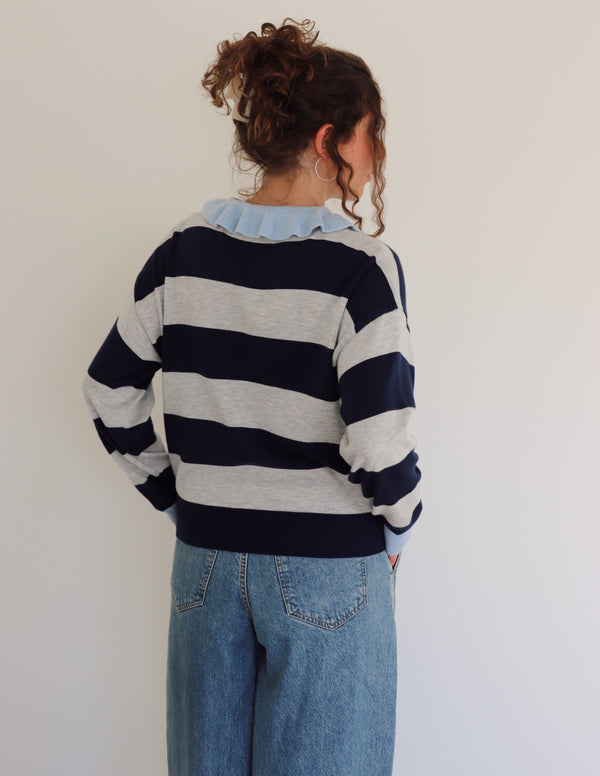 Person wearing a striped sweater and jeans against a plain background