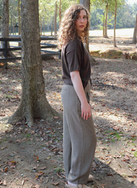 a woman wearing a chocolate brown short sleeve cardigan with brown striped pants stands in an outdoor setting