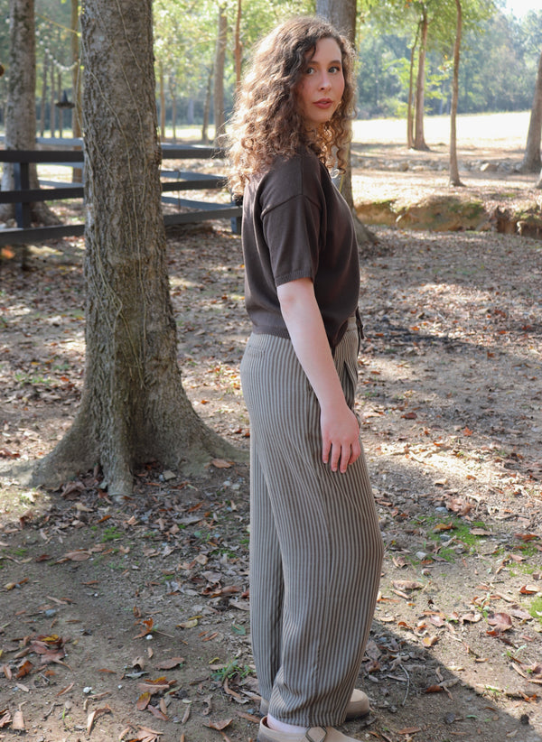 a woman wearing a chocolate brown short sleeve cardigan with brown striped pants stands in an outdoor setting