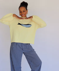 Person wearing a light yellow sweater with a fish design and striped pants against a plain background