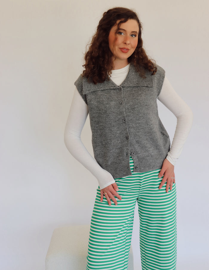 Woman wearing a gray vest over a white shirt with green striped pants against a white background