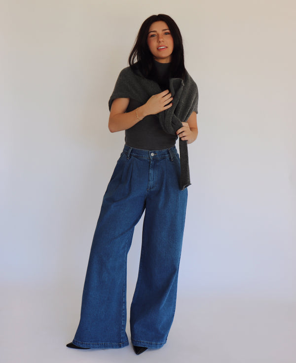 Woman wearing a dark gray turtleneck and blue jeans against a white background