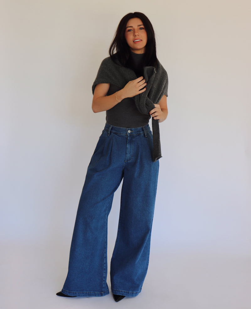Woman wearing a dark gray turtleneck and blue jeans against a white background