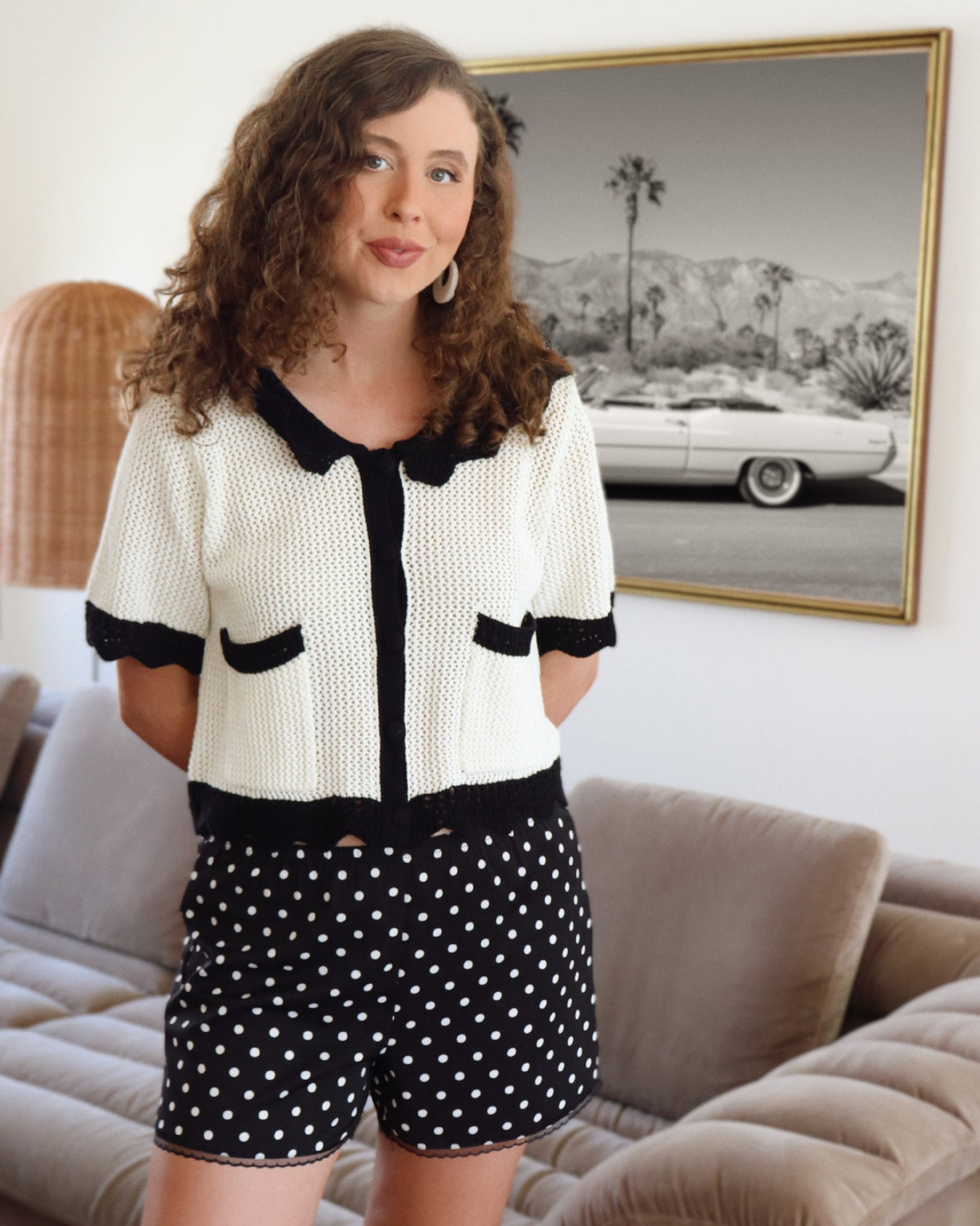 Woman wearing a black and white outfit with polka dot shorts in a living room.