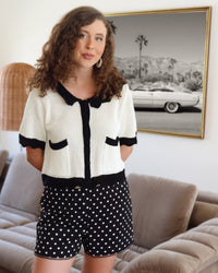 Woman wearing a black and white outfit with polka dot shorts in a living room.