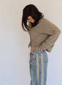 Woman wearing a taupe cardigan and blue jeans against a plain background