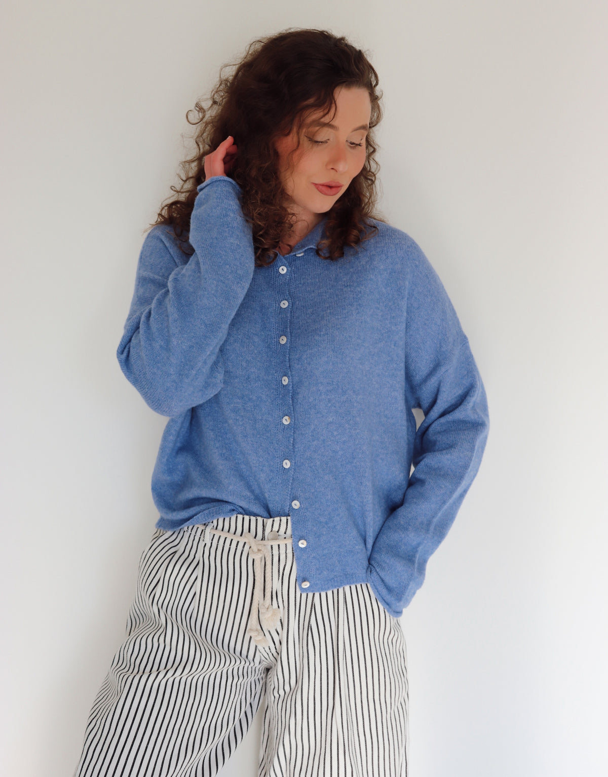 Woman wearing a blue cardigan and striped pants in front of a white wall.