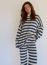 A woman wearing a matching two-piece loungewear set with blue and beige horizontal stripes, featuring a long-sleeve top and wide-leg pants, standing against a plain white background.
