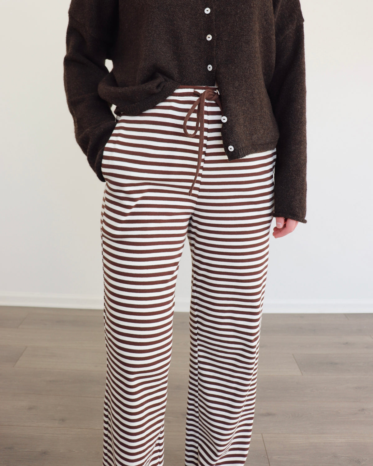 Woman wearing a chocolate brown cardigan and striped pants against a white background
