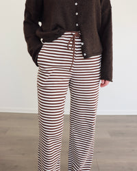 Woman wearing a chocolate brown cardigan and striped pants against a white background