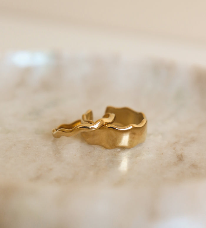 2 gold rings with wavy design on a marble surface