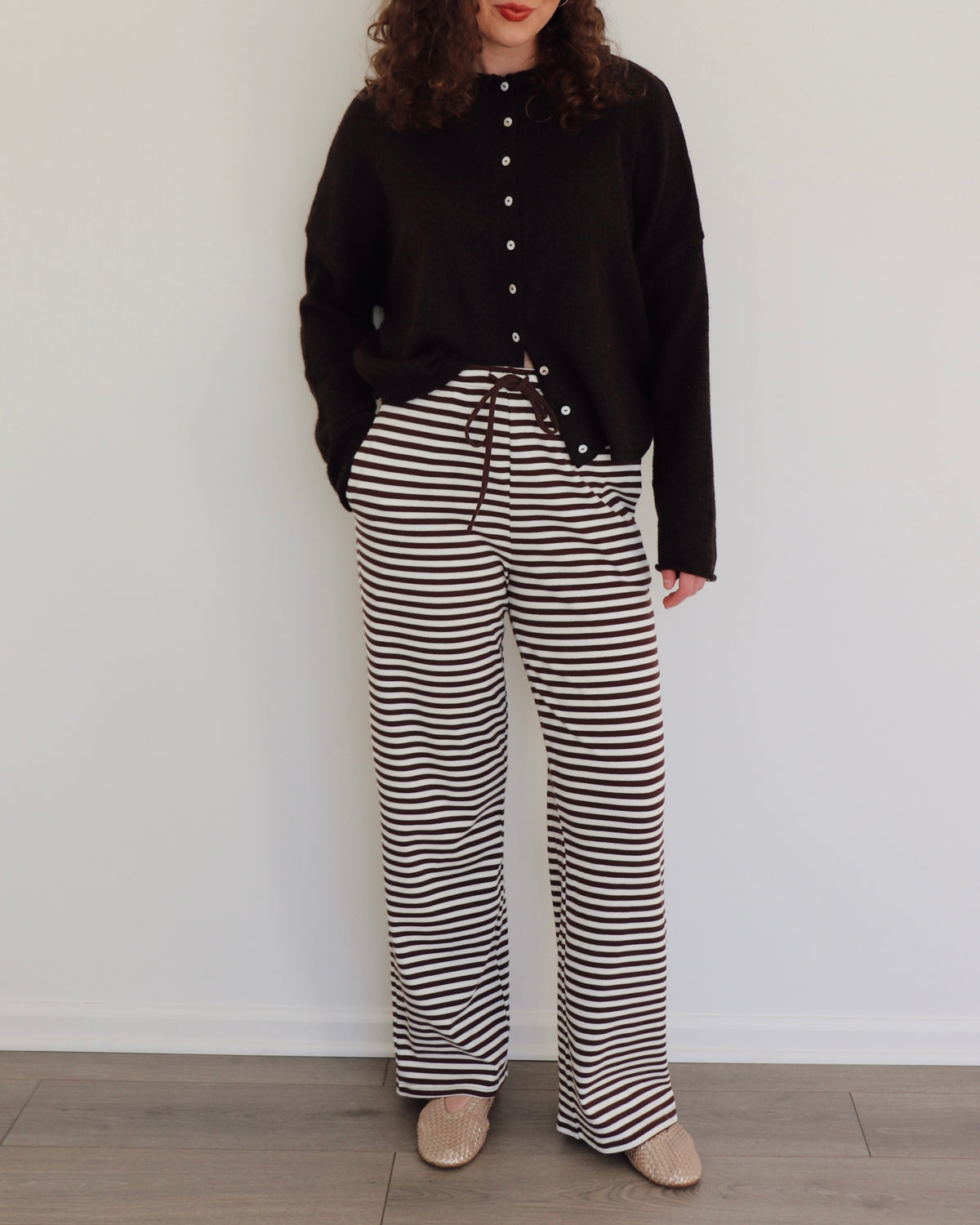 Woman wearing a chocolate brown cardigan and striped pants against a white background