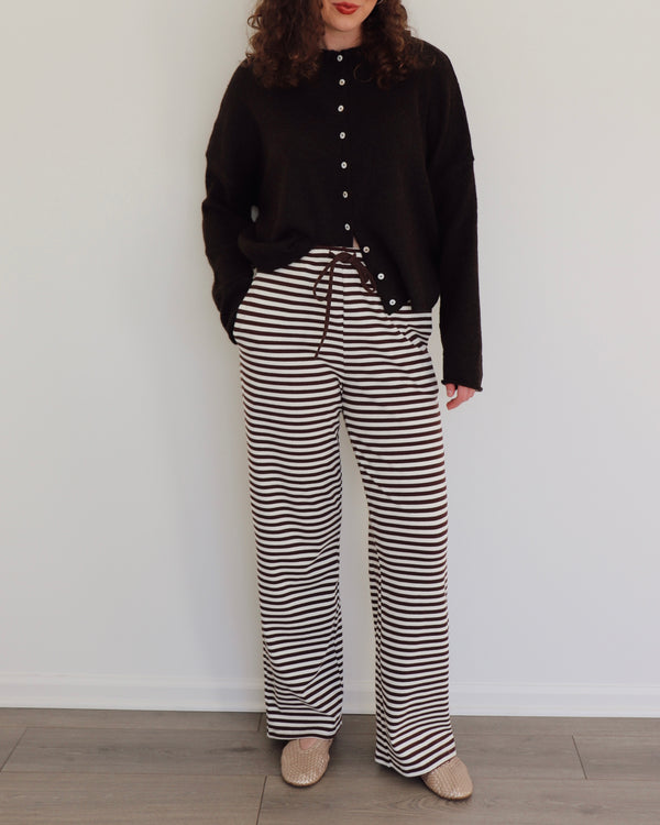 Woman wearing a chocolate brown cardigan and striped pants against a white background