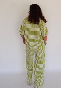 A person viewed from behind wearing a matching two-piece lounge set with short-sleeve top and wide-leg pants, both in a light green and white horizontal stripe pattern, against a plain white wall.