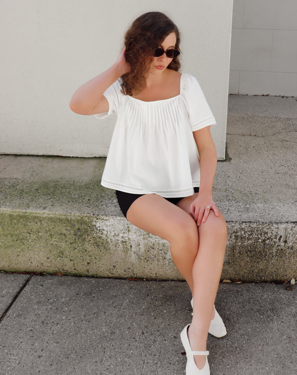 Woman sitting on steps wearing a white top and black shorts.