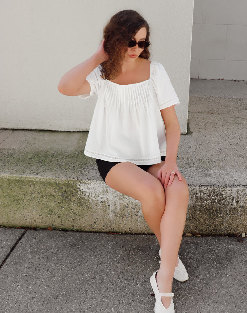 Woman sitting on steps wearing a white top and black shorts.