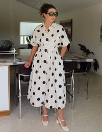 Woman wearing a white dress with black polka dots in a modern kitchen.