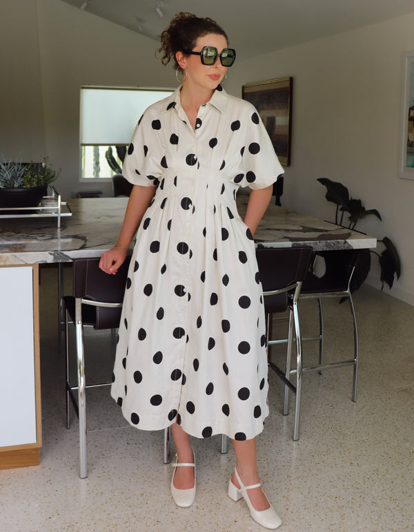 Woman wearing a white dress with black polka dots in a modern kitchen.