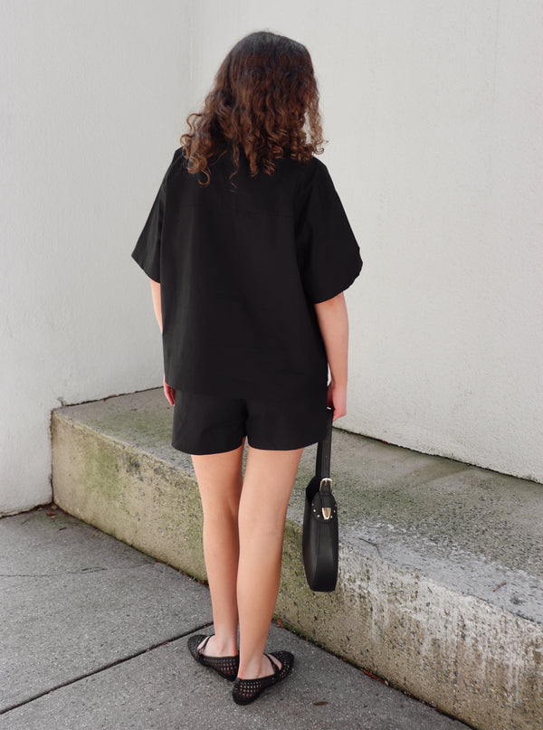 Woman in a black outfit standing on concrete background against a beige  wall.