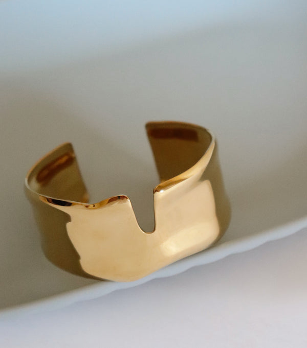 Gold cuff bracelet on a light blue and white surface 