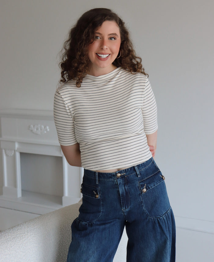 Woman wearing a striped shirt and jeans standing in a room with a white fireplace.
