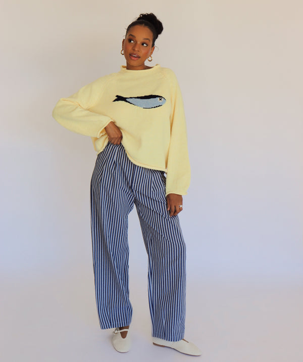 Person wearing a light yellow sweater with a fish design and striped pants against a plain background