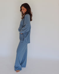 A woman modeling a matching blue striped lounge set, consisting of a long-sleeve top and wide-leg pants, against a plain white studio background.