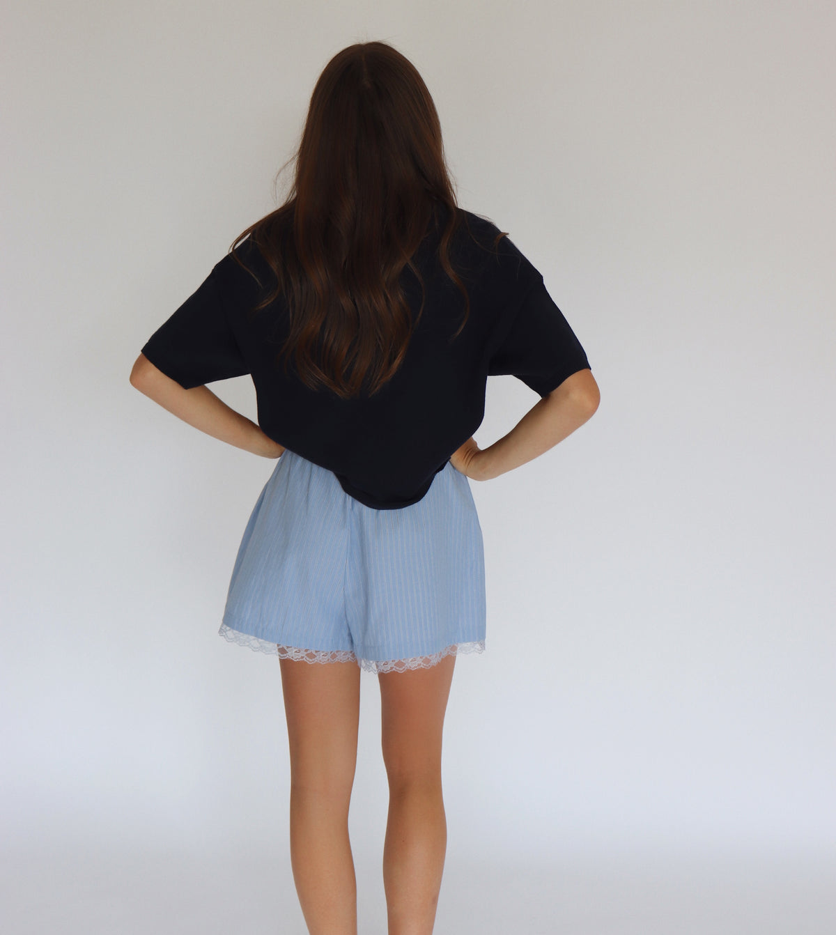Woman wearing a navy short sleeve cardigan and light blue shorts against a white background