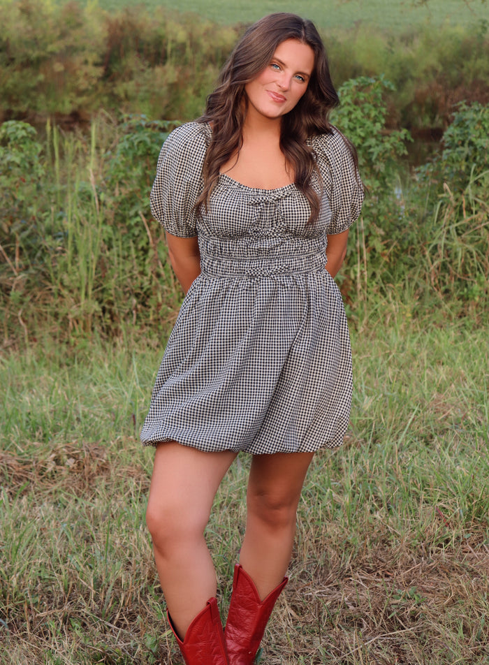 Woman in a checkered dress and red boots standing in a grassy field