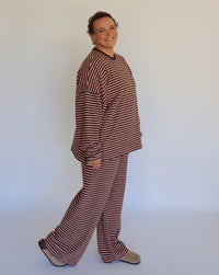 Woman wearing a brown and pink striped loungewear set in front of an off white wall.