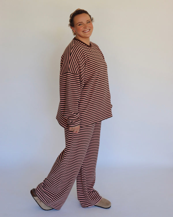 Woman wearing a brown and pink striped loungewear set in front of an off white wall.
