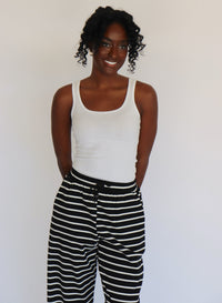 Woman wearing a white tank top and black and white striped pants on a white background
