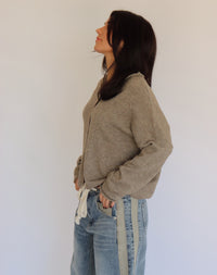 Woman wearing a taupe cardigan and blue jeans against a plain background