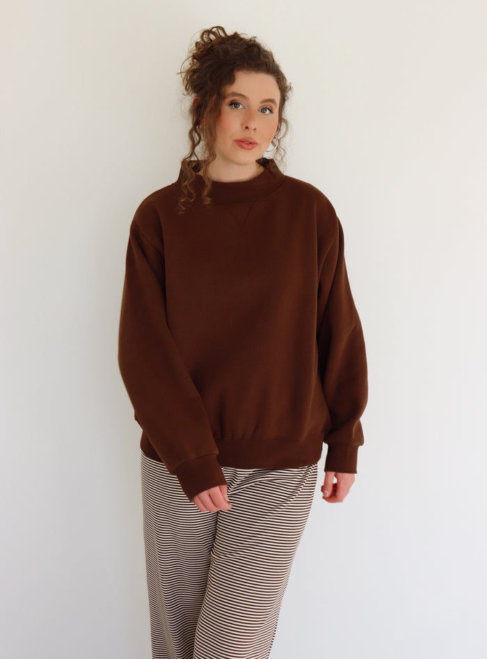 Person wearing a brown sweater and striped pants against a white background